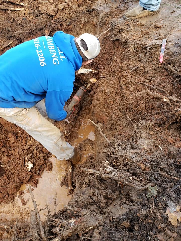 Technician cutting pipe in a muddy trench during a main-line repair